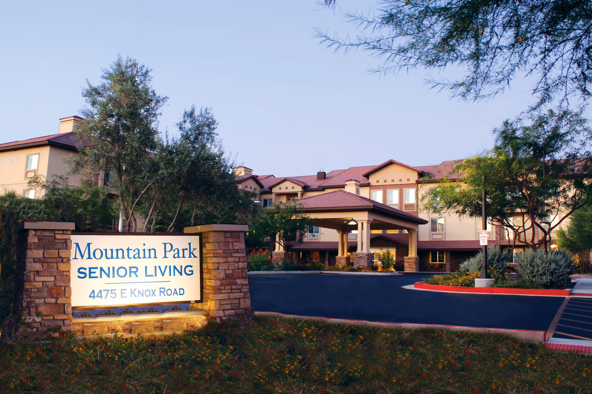 Exterior view of Mountain Park Senior Living facility with a large sign displaying the name and address, surrounded by trees and landscaping, and a multi-story building with a covered entrance in the background.