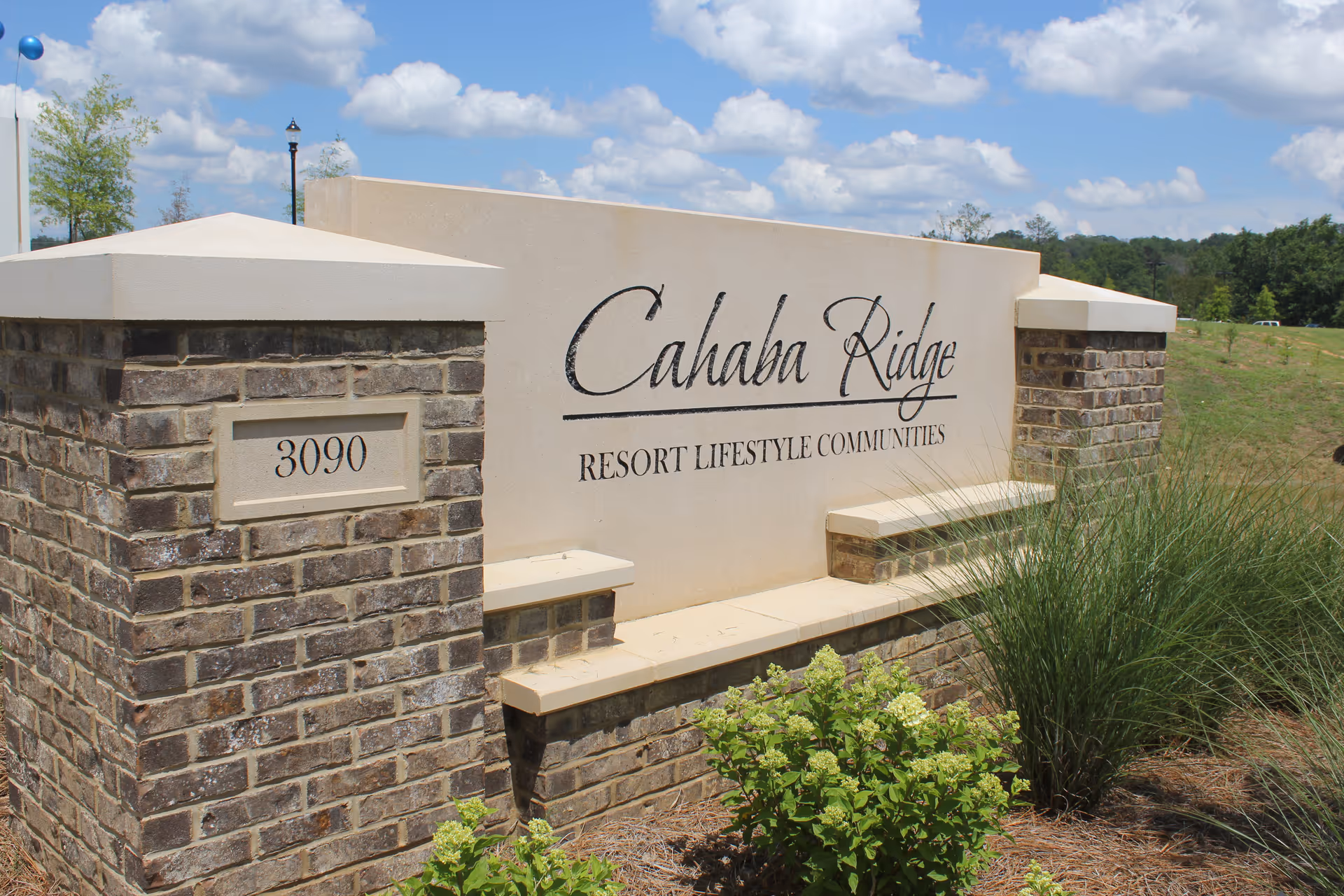 Outdoor stone and concrete sign for Cahaba Ridge Resort Lifestyle Communities with the address number 3090, surrounded by grass and plants under a partly cloudy sky.