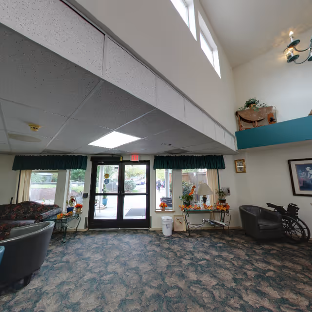 Lobby entrance of a retirement community with double glass doors, seating, decorative tables, and high ceilings.