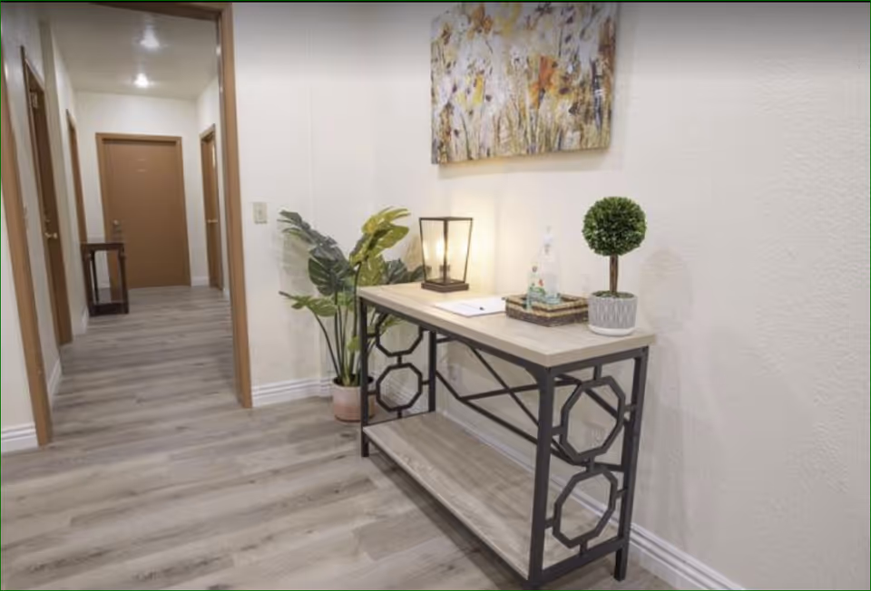 Interior hallway with a console table topped with a lamp, plants and artwork, and doors leading to rooms.