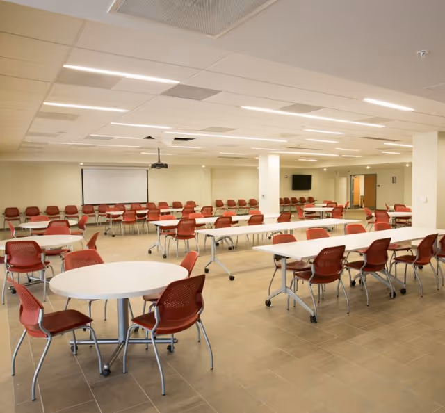 Empty senior living dining hall with red chairs and many tables.