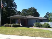 Single-story building with flagpole, shrubs, and a front entrance.