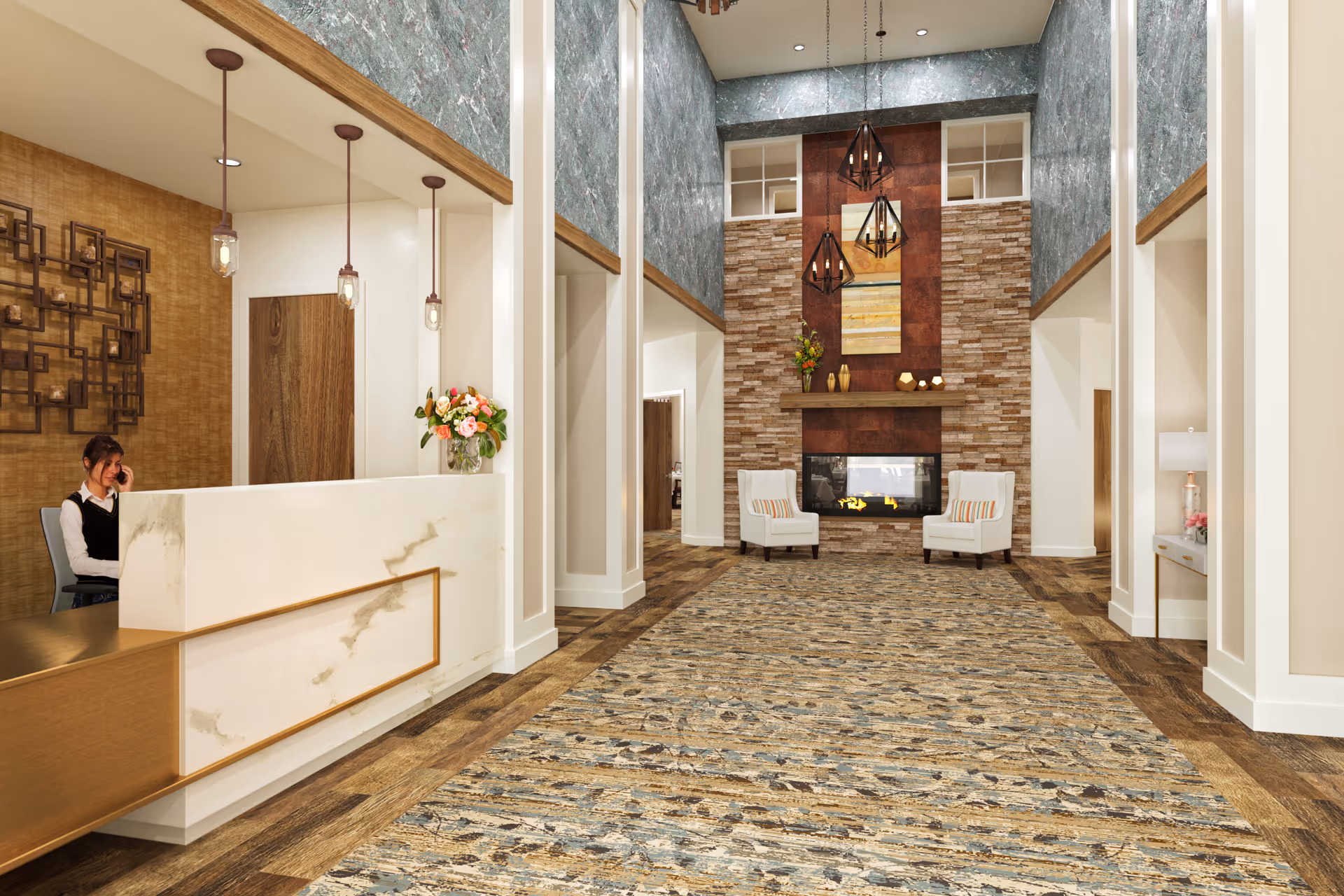 Interior view of a senior living facility lobby with a reception desk on the left where a woman is seated and talking on the phone. The space features a high ceiling, modern pendant lights, a large patterned carpet, two white armchairs in front of a stone fireplace, and decorative wall art above the fireplace.