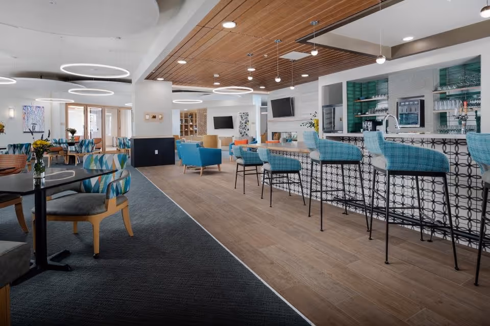 Bright modern communal lounge and bar area with turquoise barstools, seating booths and circular ceiling lights.