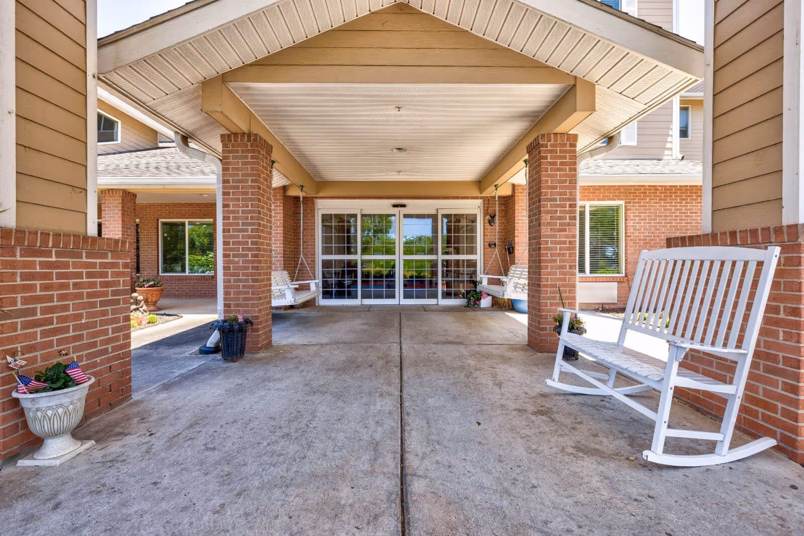 Covered entrance with brick columns, sliding glass doors, and white rocking benches at the front of the building.
