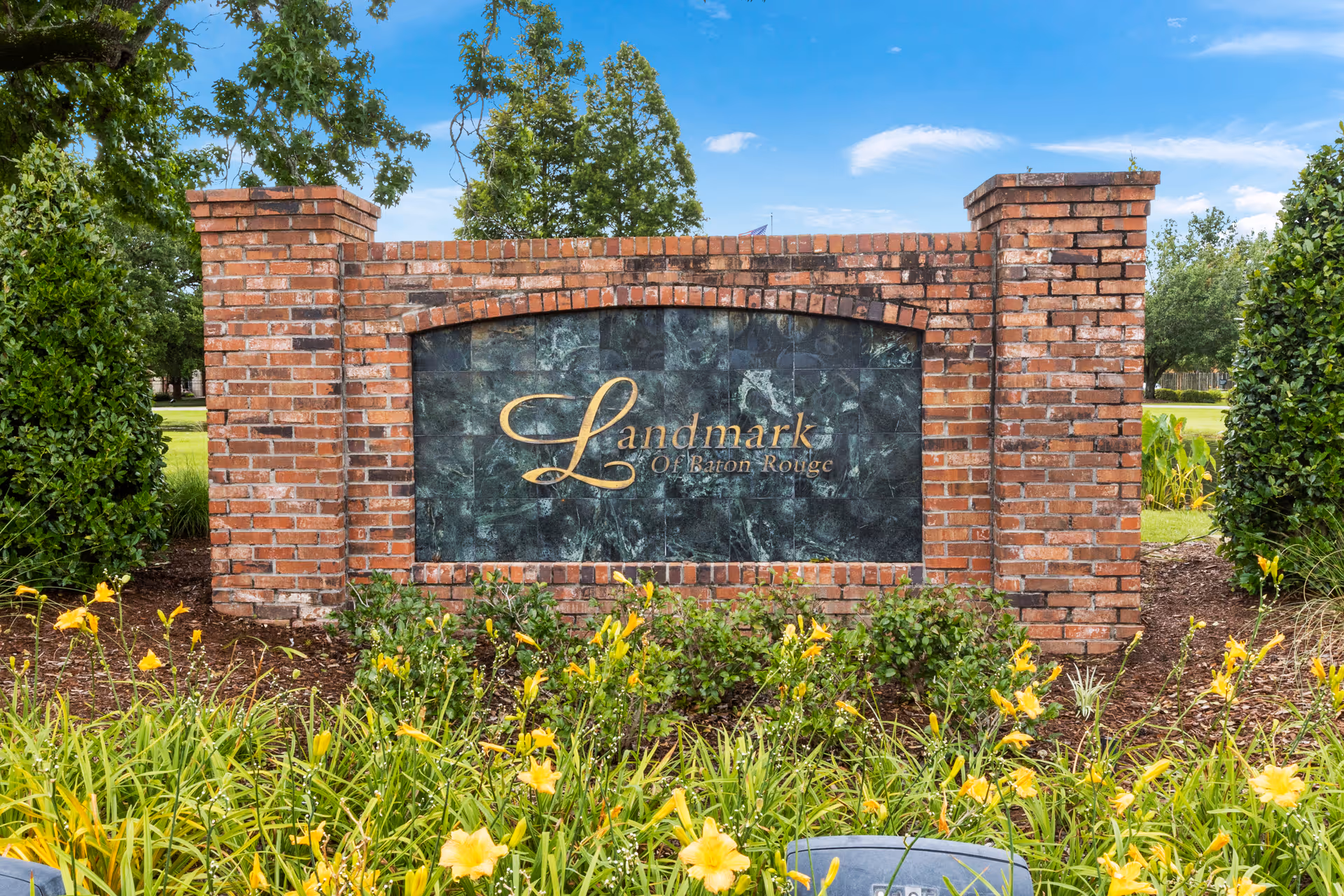 Brick entrance sign that reads Landmark of Baton Rouge surrounded by landscaping and yellow flowers.
