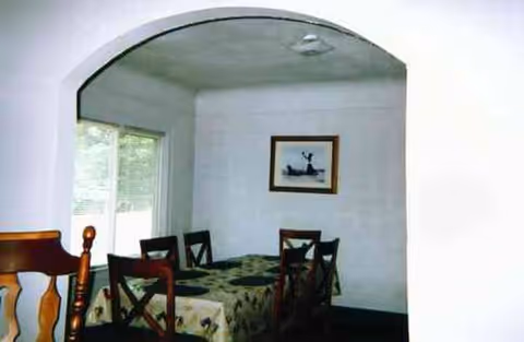 Arched doorway opens to a dining room with a table, chairs, a window, and framed art.