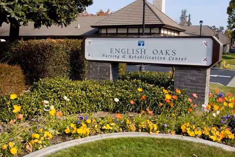 Exterior view of the English Oaks facility sign with landscaped flower beds.