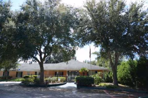 Front exterior of Haven House of Ocala, a single-story senior living facility with large trees.