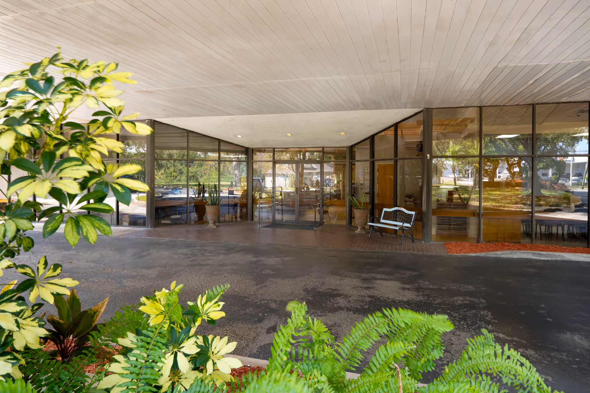 Covered entrance and drive-up area of Peninsula Health Center with glass doors, a bench, and landscaping in front.