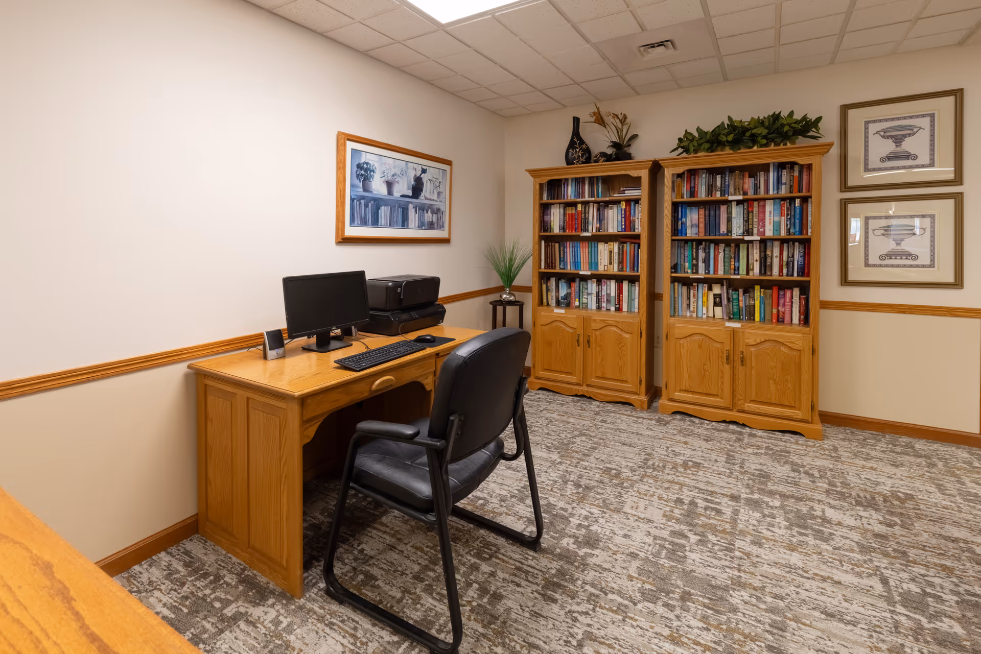 A small interior office/library with a wooden desk, computer and chair, and two wooden bookshelves filled with books.