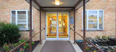 Front entrance of a brick senior living building with glass doors and a ramp.