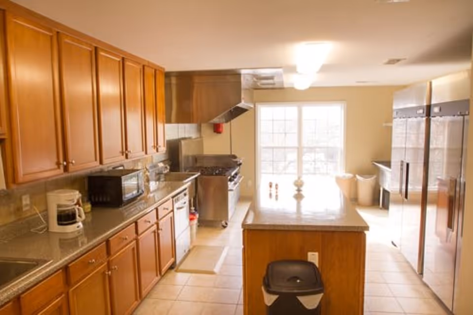 Bright communal kitchen with wooden cabinets, a center island, stainless steel range and refrigerators, and countertop appliances.