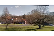 Front exterior of a two-story brick health and rehabilitation building with a grassy lawn, several trees, and parked cars.