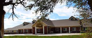 Brick senior living facility exterior with a covered entrance and lawn.