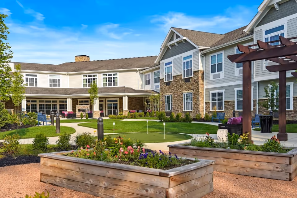 Outdoor courtyard of a senior living community with raised wooden planters, a putting green, seating areas and the two-story building exterior.