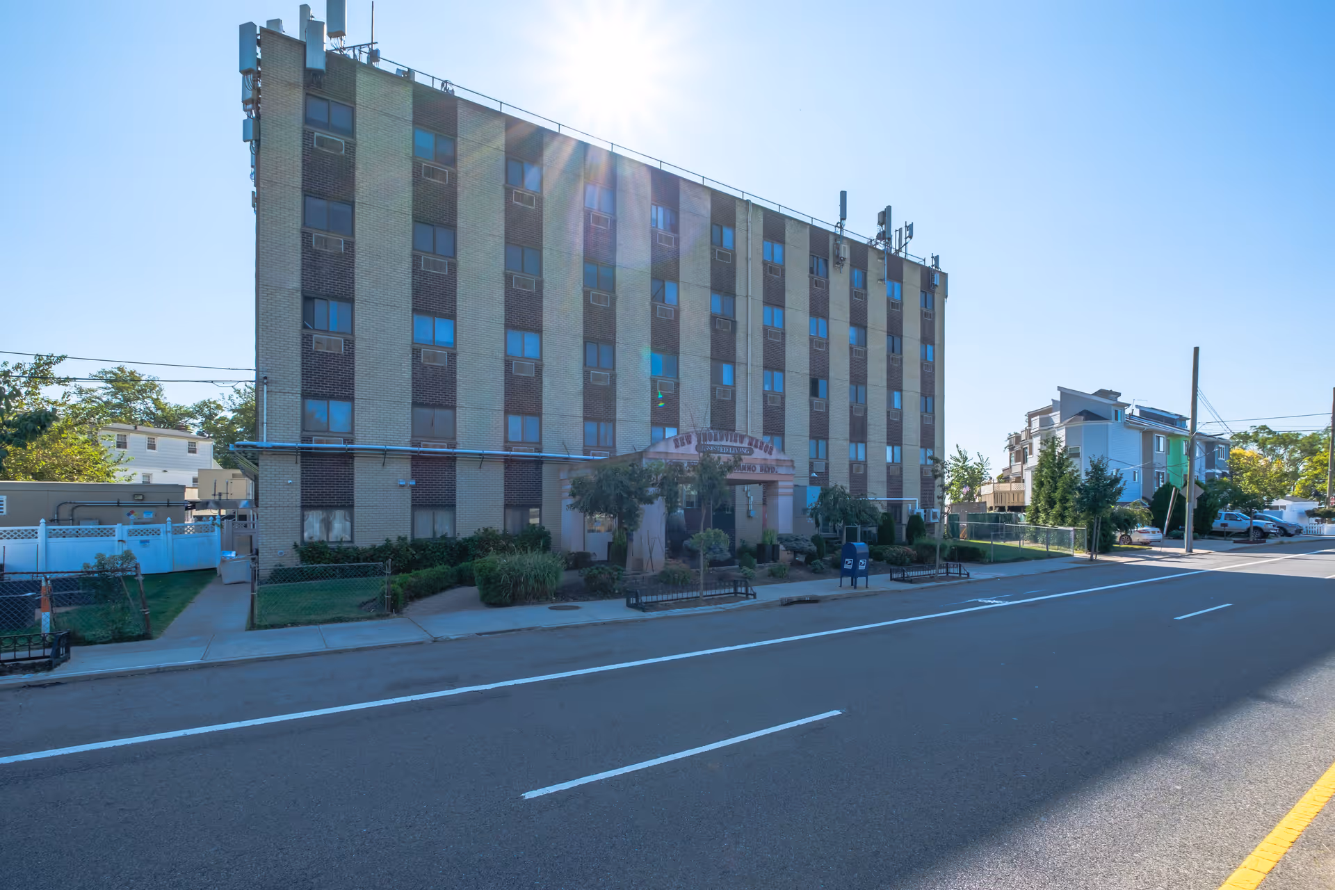 Exterior view of a multi-story senior living facility named New Broadview Manor on a sunny day, with a clear blue sky and a street in the foreground.