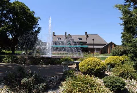 Front view of Franciscan Manor with a fountain and manicured landscaping.
