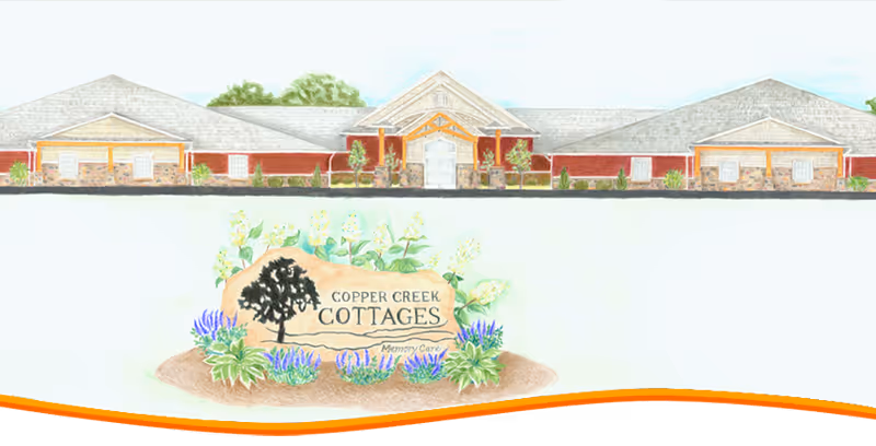 Illustration of a single-story building with a peaked roof and multiple sections, surrounded by greenery. In front of the building is a landscaped area with a large stone sign that reads 'Copper Creek Cottages Memory Care' with decorative plants and flowers around it.