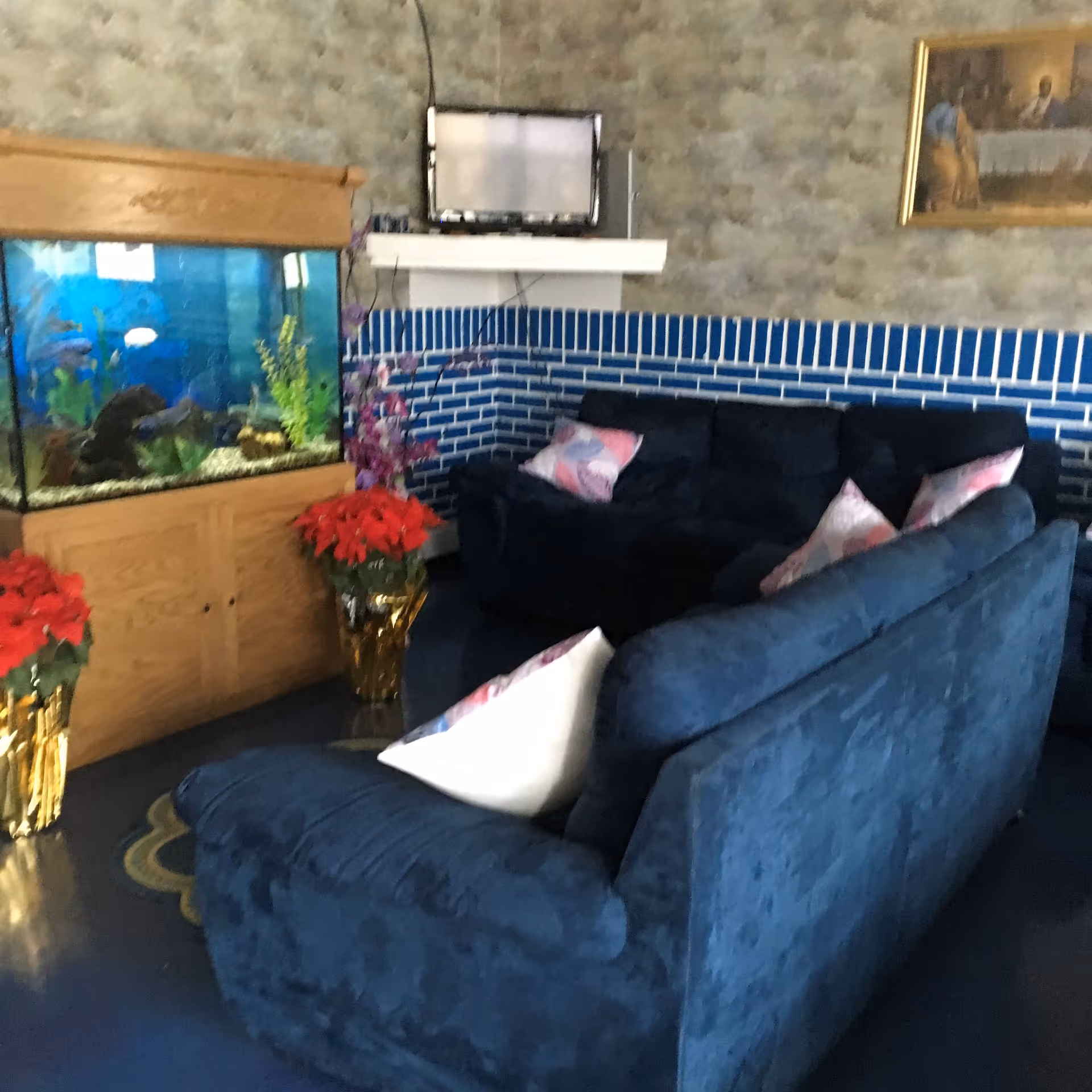 A lounge area with navy blue sofas, decorative pillows, a large fish tank and a small wall-mounted TV against a blue-tiled wall.