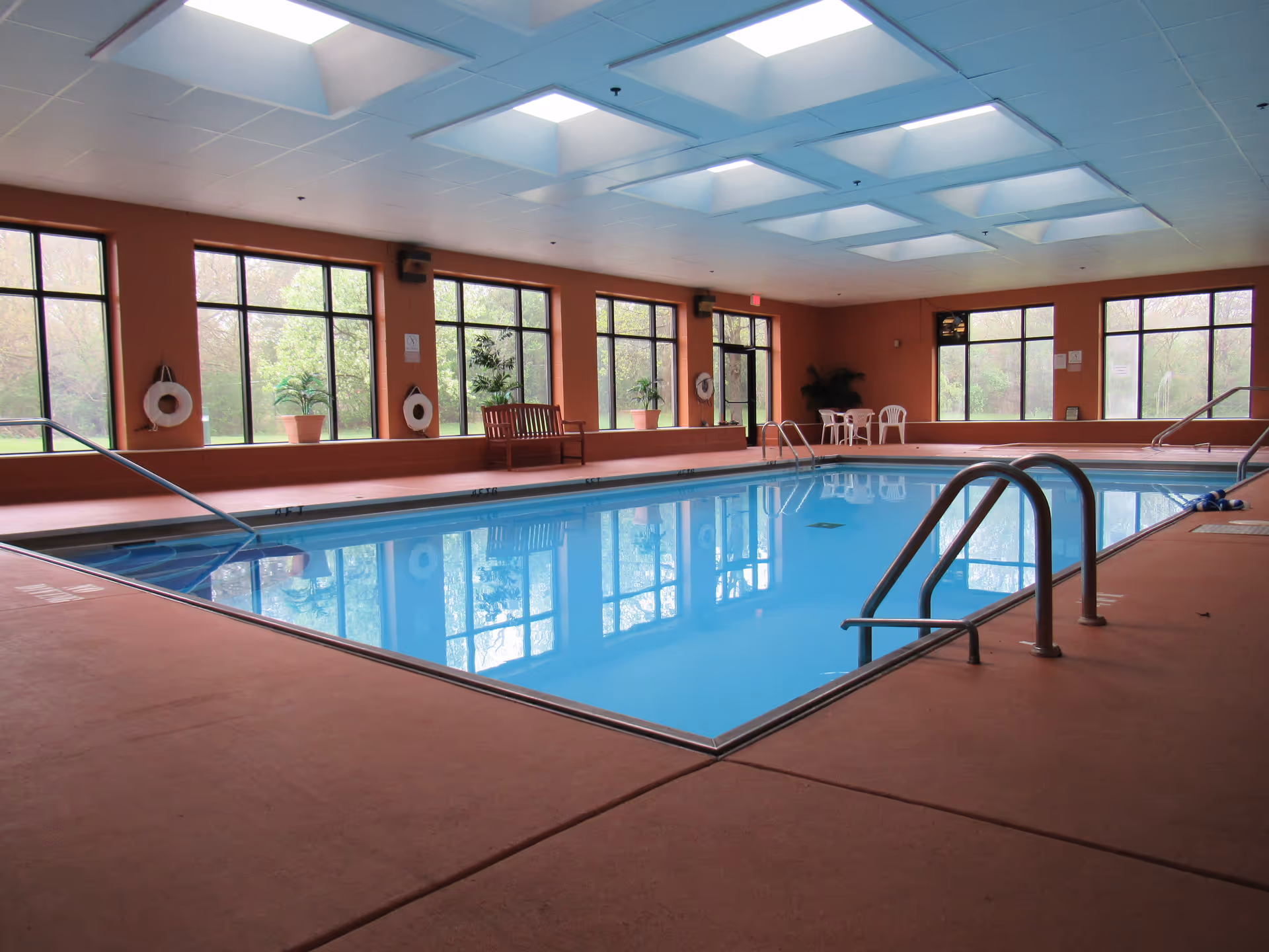 Indoor swimming pool with skylights, large windows, seating and handrails in a senior living facility.