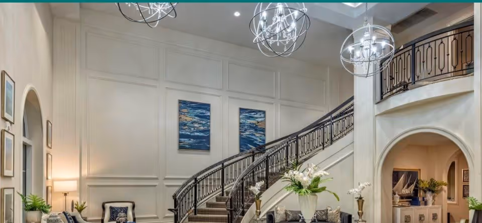 Elegant two-story lobby with a sweeping curved staircase, chandeliers, seating areas, plants and wall art.