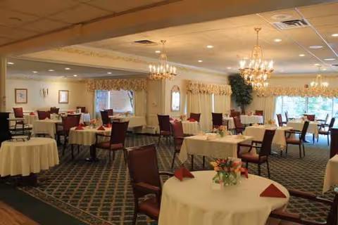A senior living dining room with round tables, chairs, and chandeliers.