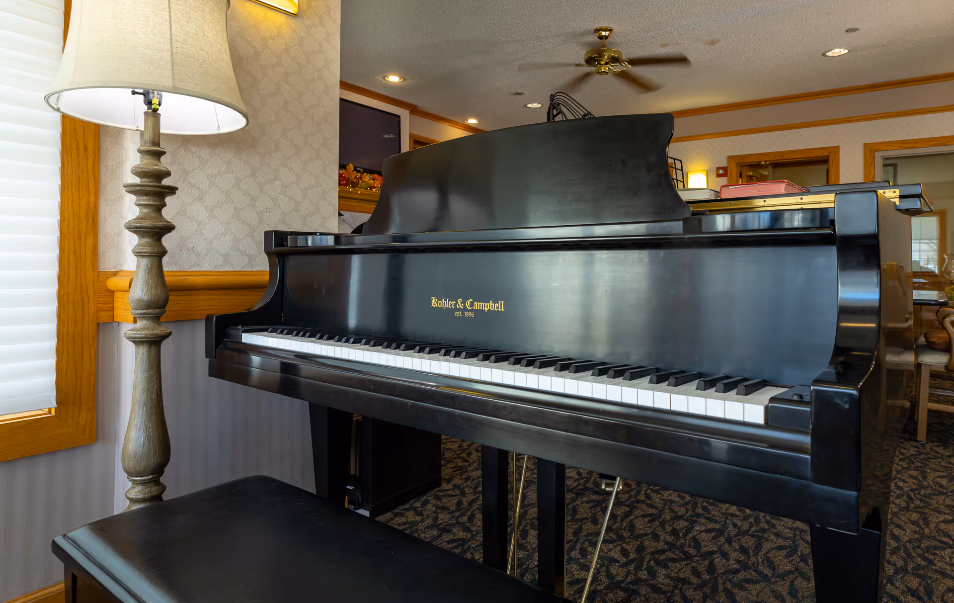 Black grand piano and bench in a furnished common room next to a floor lamp and seating.