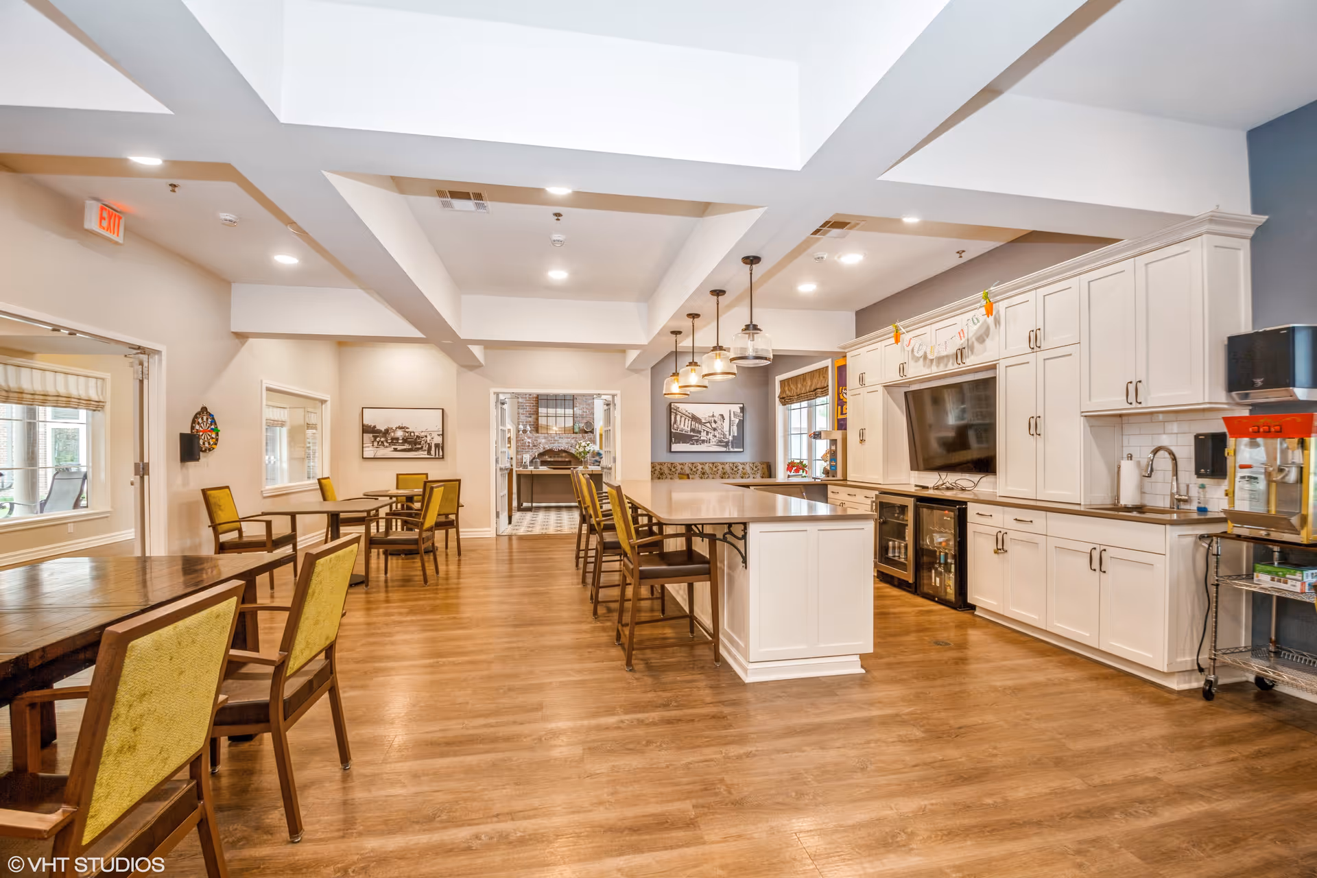 Open dining room and kitchen area with wooden tables and green-upholstered chairs, a central island, and white cabinetry.