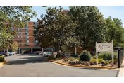 Exterior view of Culpepper Garden senior living facility with a multi-story brick building, trees, parked cars, and a sign displaying the facility's name near the entrance.