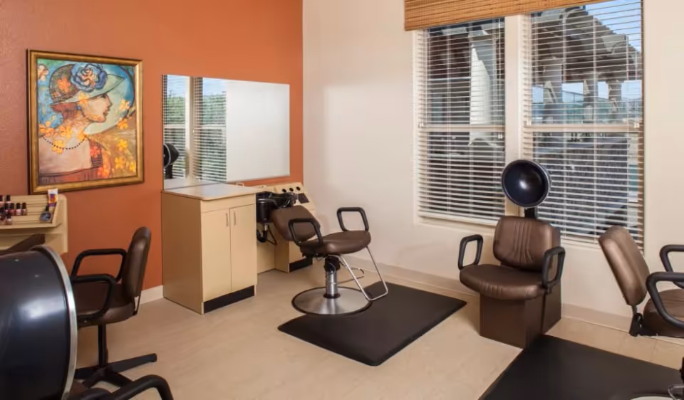 Interior salon room with brown styling chairs, a hooded hair dryer, a mirror, and a window with blinds.