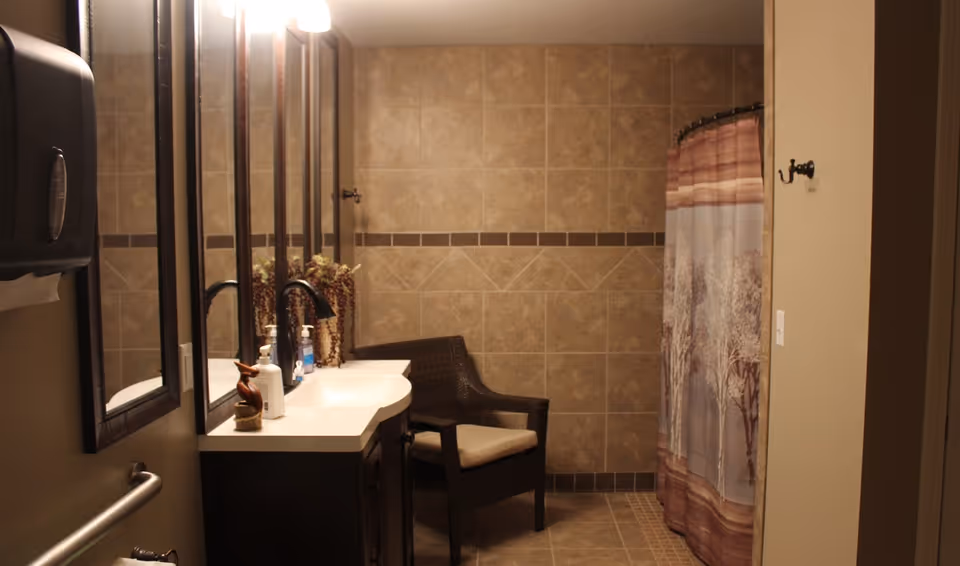 Tiled bathroom featuring a vanity with mirror, a wicker chair, and a shower with a patterned curtain.