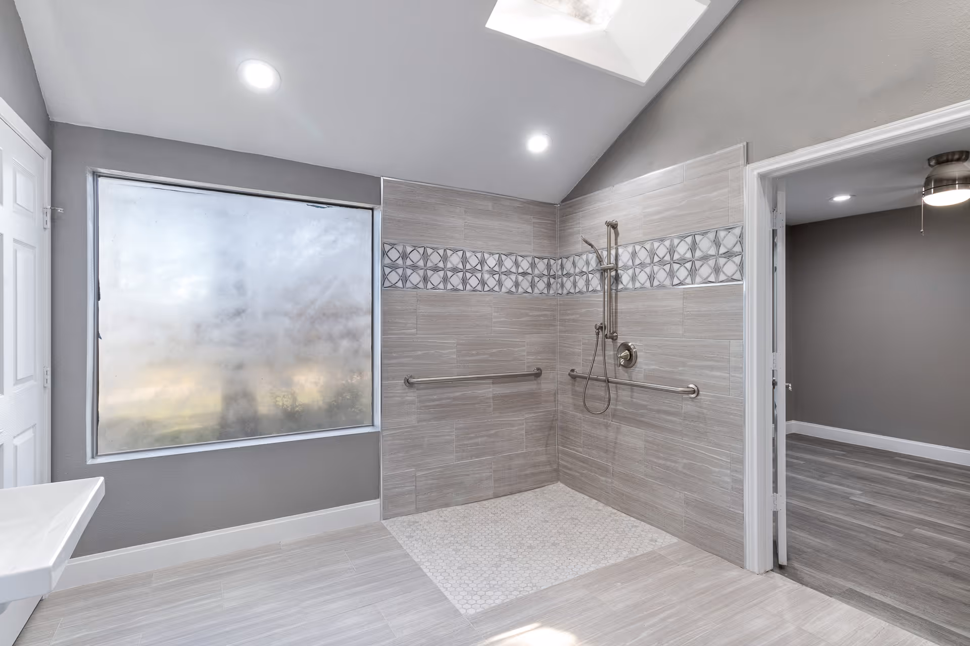 Accessible bathroom with a roll-in tiled shower, grab bars, frosted window, and gray tile flooring.