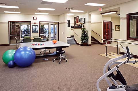 Spacious activity and physical therapy room with exercise balls, a therapy table, parallel bars, and seating.