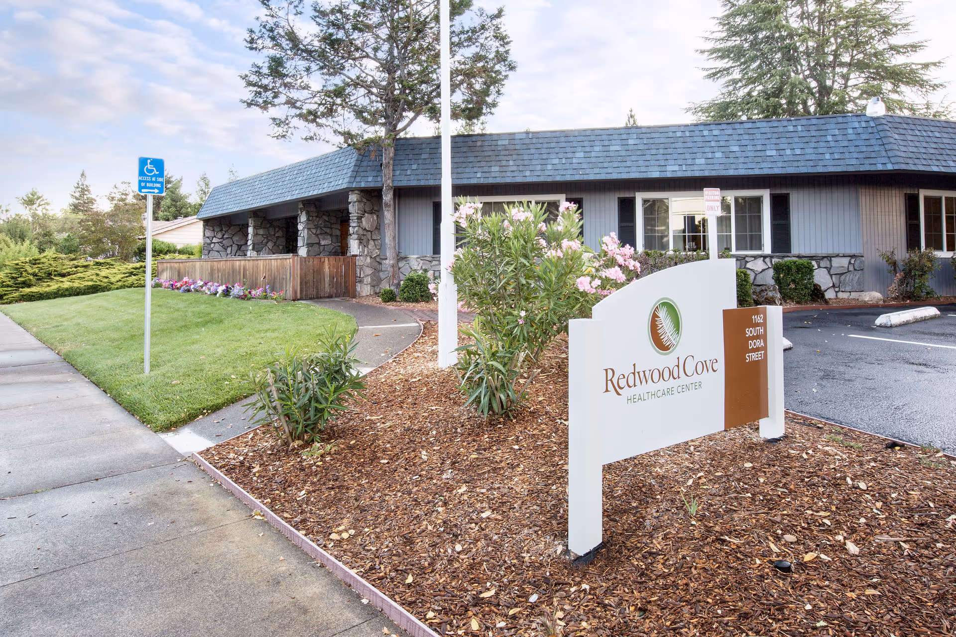 Front exterior of Redwood Cove Healthcare Center showing the building, landscaping, parking area, and a prominent entrance sign.