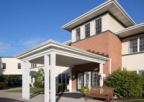 Facade of GreenField Court senior living facility with a covered entrance and bench.