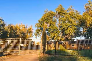 Gated entrance to a senior living facility with trees and a sunny sky.