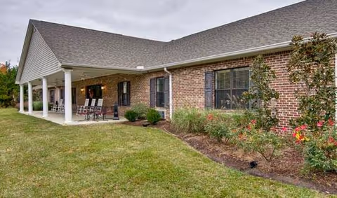 Single-story brick building with a covered porch, lawn, and shrubs.