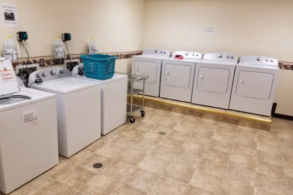 Laundry room with multiple washing machines and dryers, a teal laundry basket and a small rolling cart.