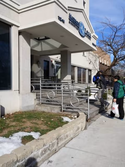 Front entrance of Madison York Assisted Living with two people approaching the accessible ramp.