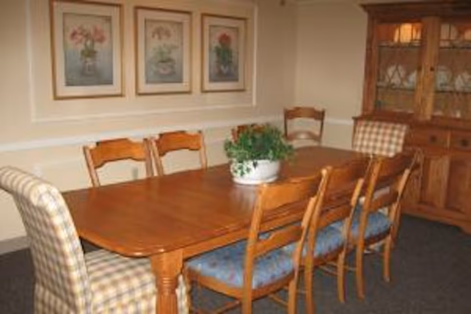 Wooden dining table with multiple chairs, a potted plant centerpiece, framed floral prints on the wall, and a china cabinet in a traditional dining room.
