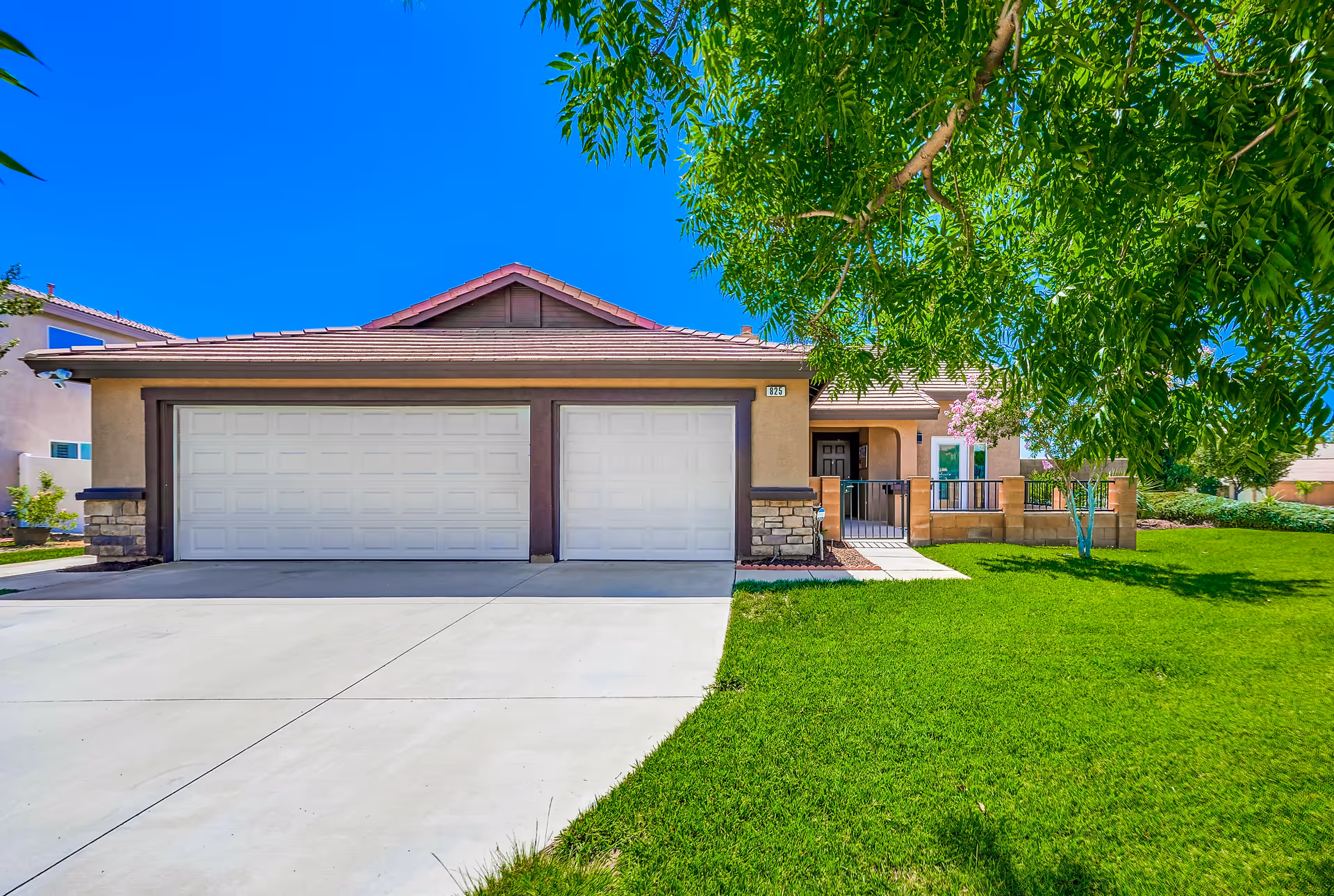 Front view of a single-story house with a three-car garage, driveway, green lawn and a large tree.