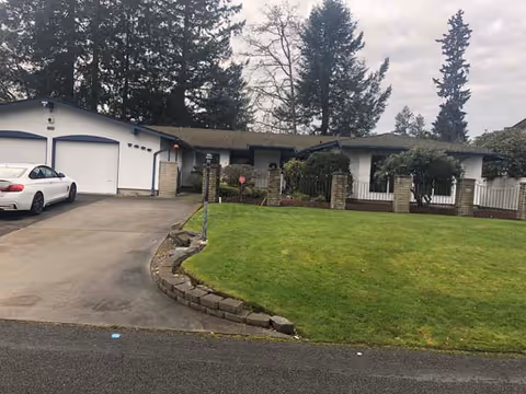Front exterior of a single-story senior living facility with a driveway, car, and lawn.