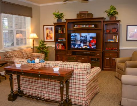 Cozy living room with plaid sofas, a wooden console table, armchairs, and a large entertainment center with a TV.