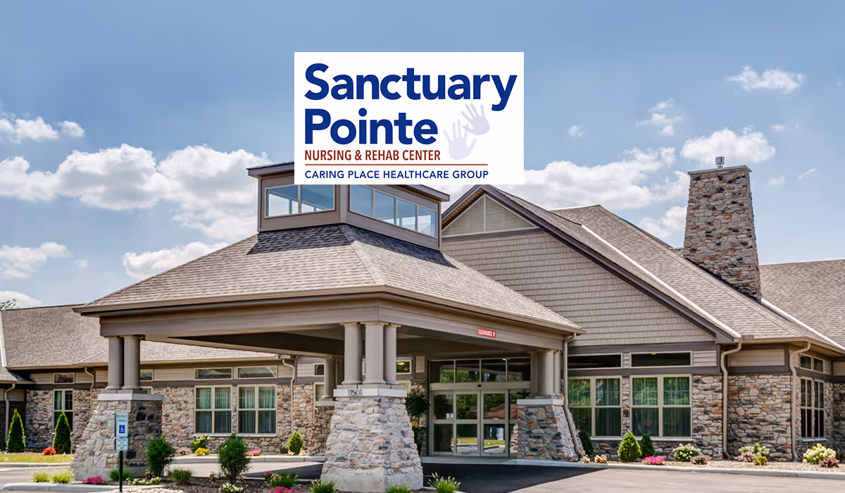 Exterior view of Sanctuary Pointe Nursing & Rehab Center building with stone and wood siding, a covered entrance supported by stone pillars, and a clear blue sky with some clouds.