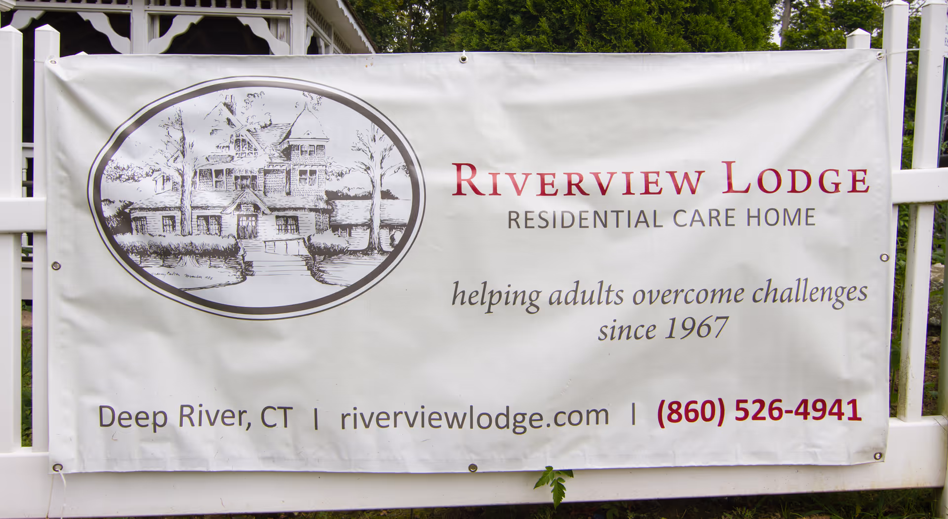 A large outdoor banner reading "Riverview Lodge Residential Care Home" with a sketch of a house and contact information.