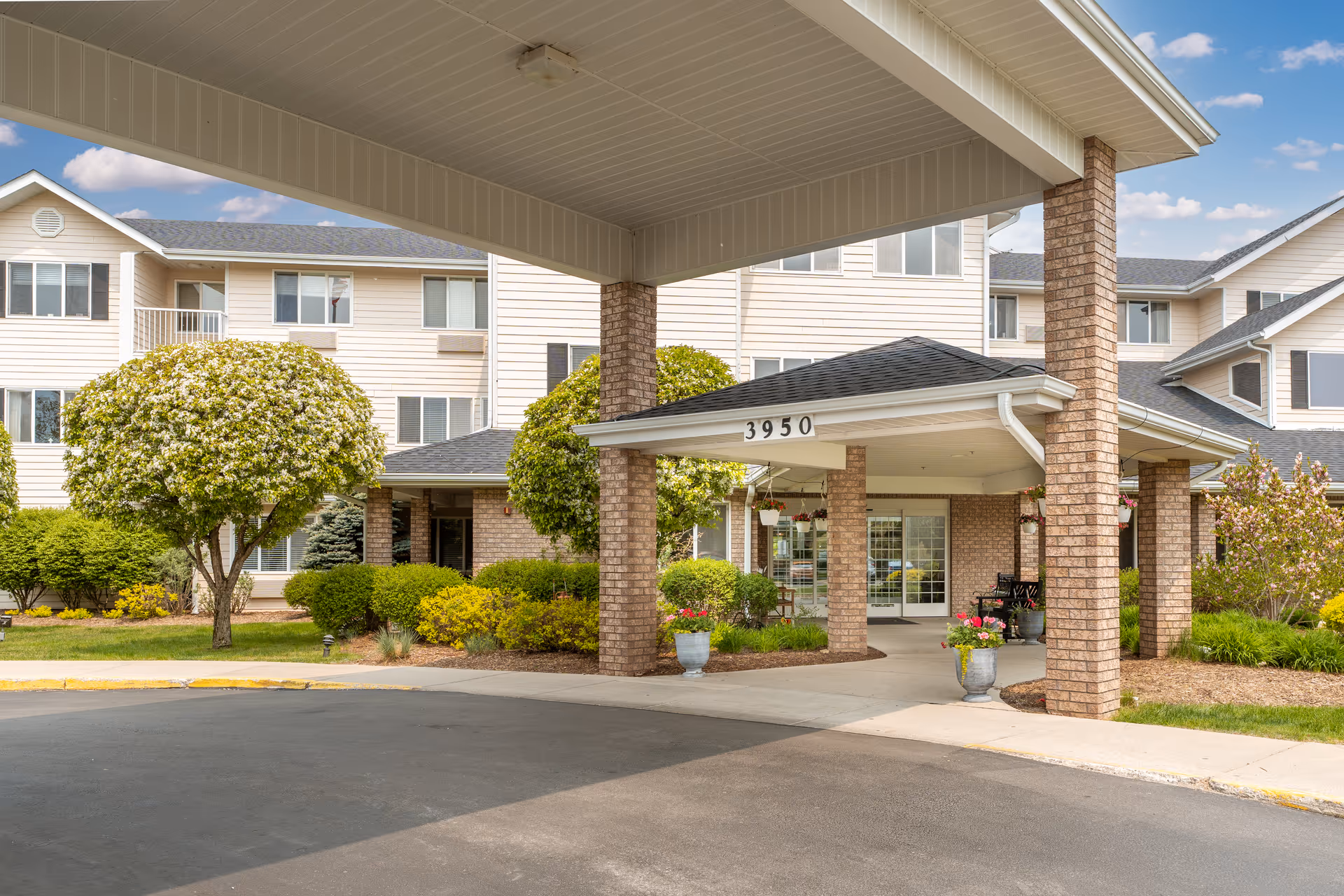 Covered porte-cochere and main entrance of a multi-story senior living building with landscaped shrubs and the address number 3950.