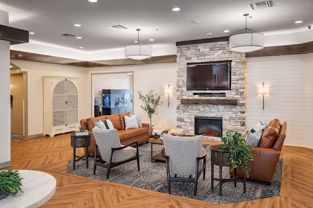 Comfortable communal lounge with sofas and armchairs arranged around a stone fireplace and wall-mounted TV.