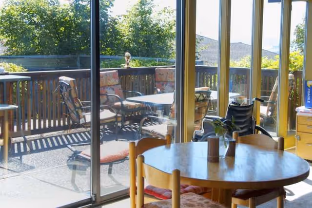 Inside a dining room with a round table and glass doors opening to a sunny balcony.