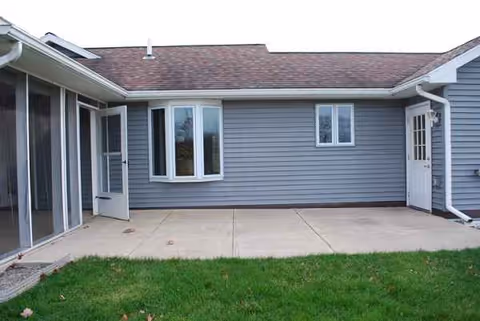 Blue single-story senior living facility exterior with a concrete patio and sliding doors.